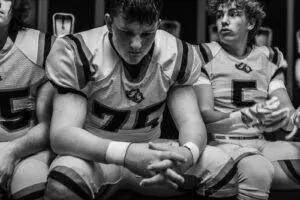 High school football players in a locker room showing focus and determination before a game.