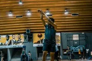 A basketball player takes a shot during practice in an indoor gymnasium setting.
